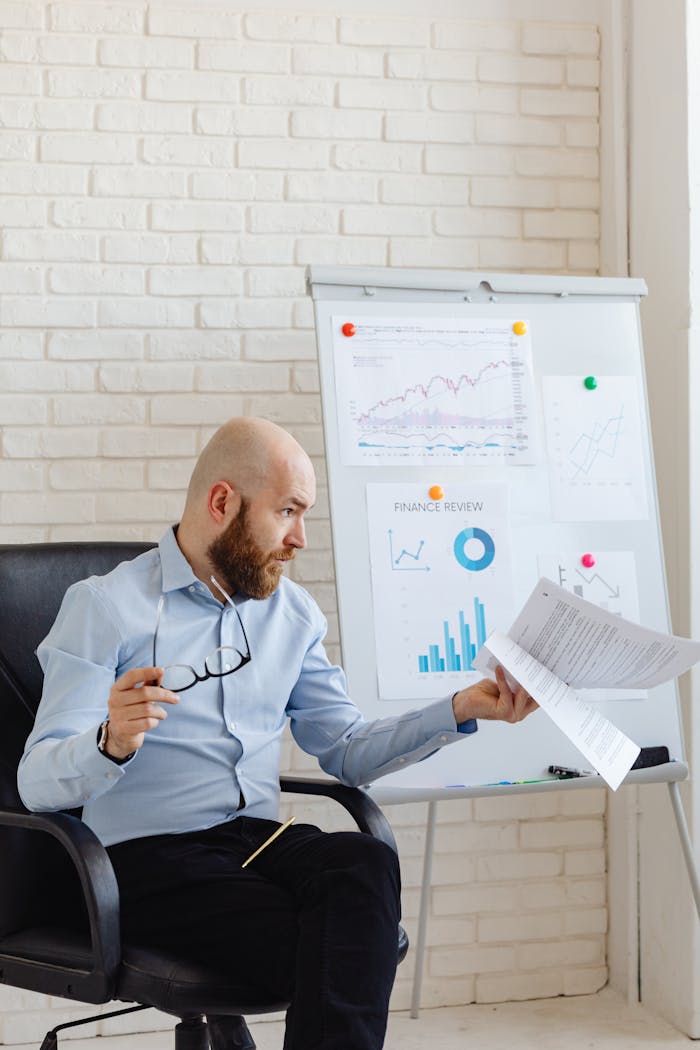 A bald businessman reviewing financial charts and documents in an office setting.