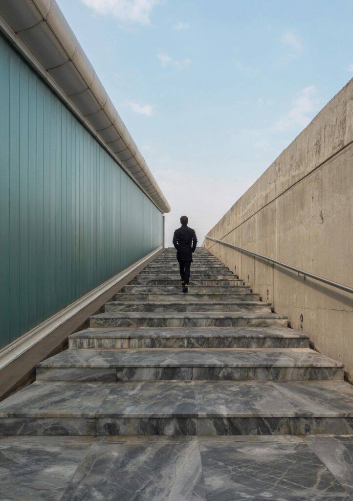 A lone business professional walks up a modern staircase under a clear sky.